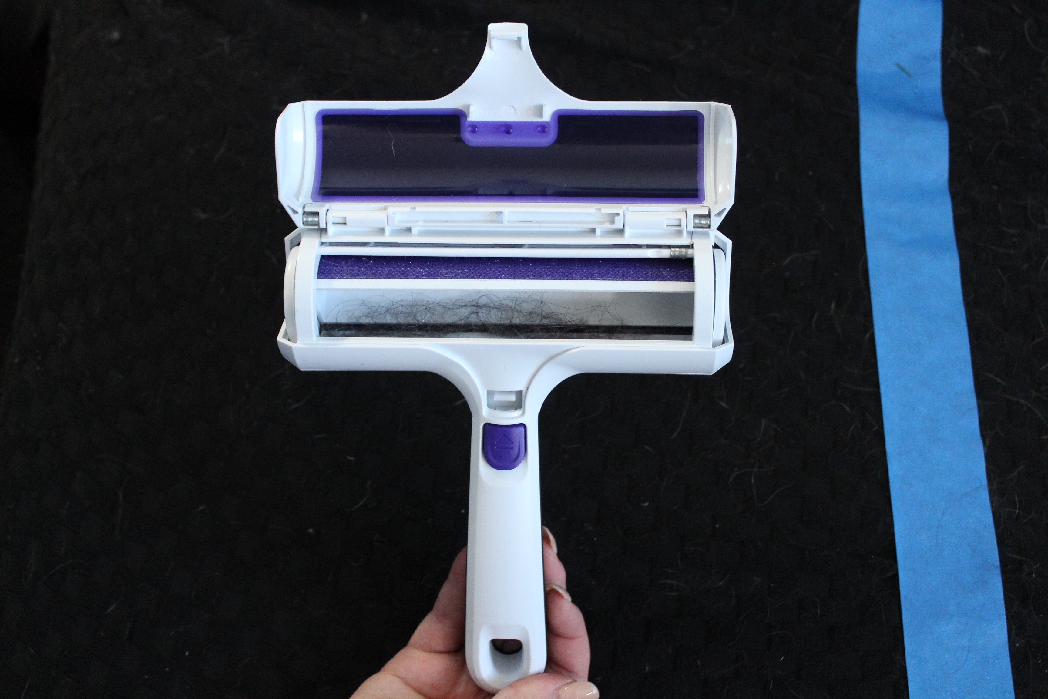 Black+Decker pet hair remover with the dust bin popped open, showing pet hair collected on the roller inside the chamber