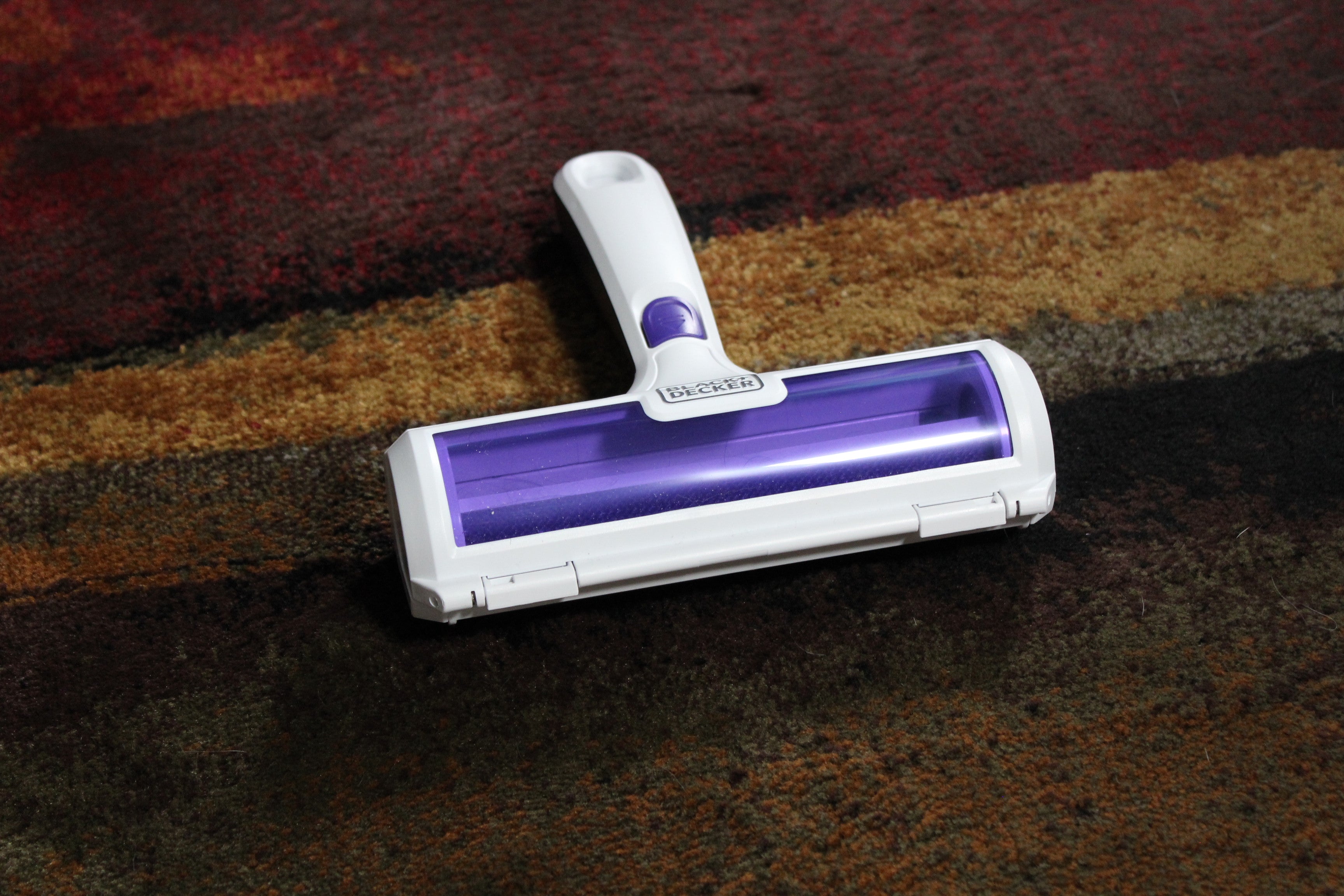 Black+Decker pet hair remover, 3/4 angle view showing the white plastic housing, purple roller, and brand logo