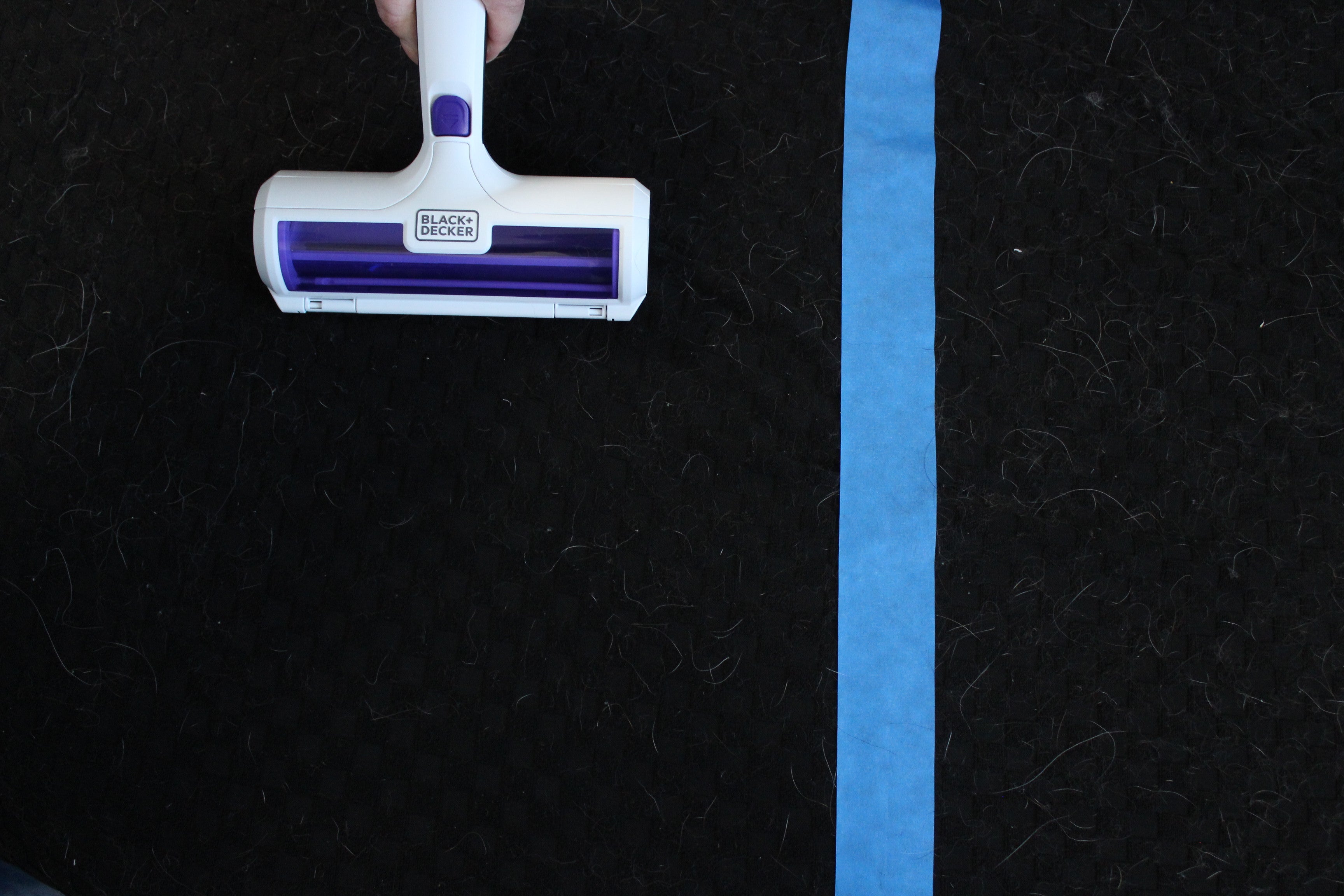 Black+Decker pet hair remover on a hair-covered black fabric surface, with blue painter's tape marking the test zone