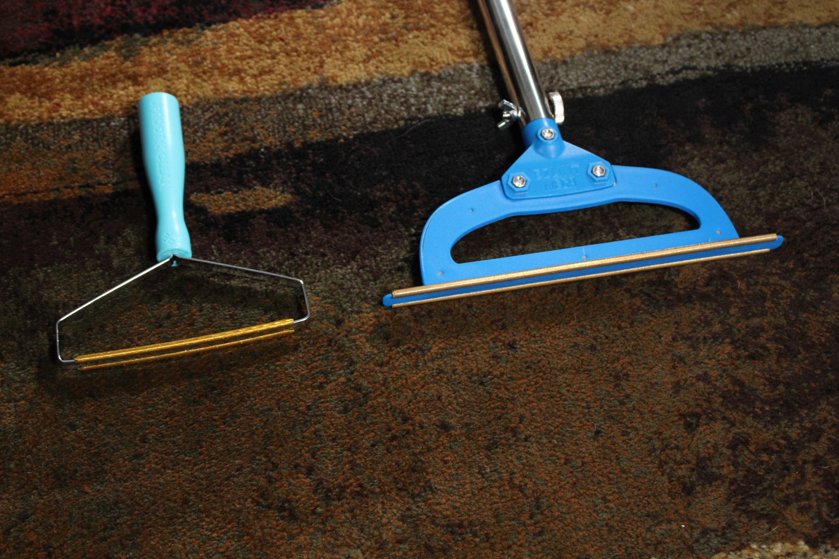 Compact handheld carpet rake on the left next to the wider PetLovers EzLint Mega carpet rake on the right, shown side by side to compare head width and handle design